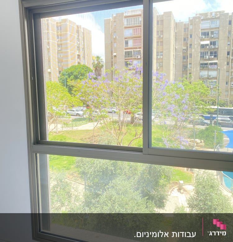 חלון אלומיניום עם נוף חיצוני של עצים ובניינים